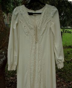 "Today I have for you a lovely 1969 Romance/Ren style Gunne Sax dress of medium to heavyweight, raw cotton that is accented with floral and heavyweight, crocheted lace. This design was often used as a wedding dress in that era and would suffice as one today. The condition is excellent and the craftsmanship is superb. It all starts with the tie bodice that is covered with a lace that consists of individual flowers within a free formation (also to be found on the attached apron). Heavy, durable la Bohemian Cotton Dress With Lace Collar, Fitted Cotton Lace Dress With Crochet Trim, Fitted Dress With Crochet Trim In Cotton Lace, Cream Cotton Dress With Crochet Trim, Vintage Fitted Dresses With Crochet Trim, Vintage Cotton Dress With Lace Cuffs, Fitted Cotton Dress With Lace Work, Long Sleeve Cotton Dress With Lace Cuffs, Long Sleeve Cotton Dress With Lace Work