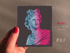 a woman's hand holding up a cross - stitch photo of herself in pink and blue