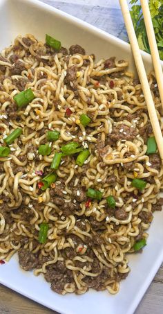 a white plate topped with noodles and meat next to chopsticks on a wooden table