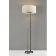 a floor lamp with a white shade on it's side and a grey wall in the background