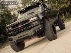 a large black truck parked on the side of a road next to trees and bushes