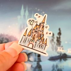 a hand holding up a sticker with a castle on it's side in front of a blurry background