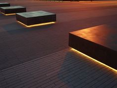 some benches are lit up at night on the pavement in front of an empty parking lot