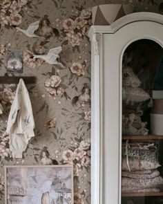 a room with floral wallpaper and pictures on the wall next to a china cabinet