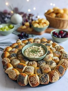 a platter filled with rolls and dip surrounded by bowls of fruit on the table