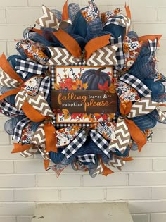 a fall wreath hanging on the side of a brick wall with an orange and blue bow