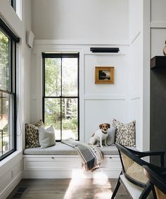 a dog sitting on a window seat in a room with white walls and wood floors