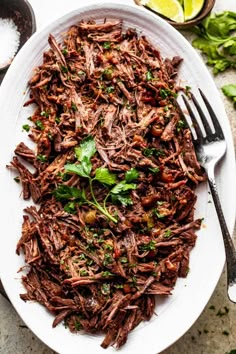 a white plate topped with shredded beef and garnished with cilantro