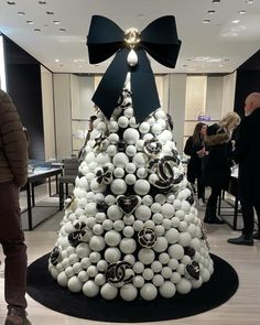 a christmas tree made out of white balls and black bows with people looking at it