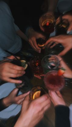 a group of people sitting around a table with drinks and wine glasses in their hands