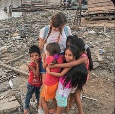 a group of children hugging each other in front of a body of water with garbage all around them