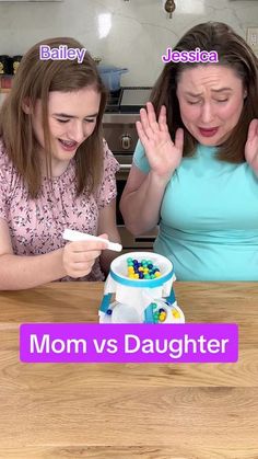 two women sitting at a table with a cake in front of them that says mom vs daughter