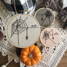 three embroidery hoops with spider web designs on them and a pumpkin next to it