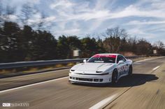 a white sports car driving down the road with trees in the backgrouund