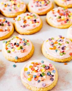 cookies with pink frosting and sprinkles are on a baking sheet, ready to be eaten