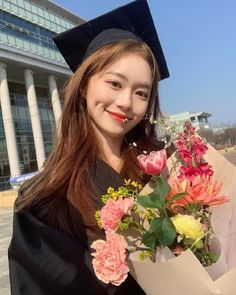 a young woman in graduation gown holding flowers