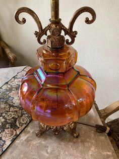 an orange vase sitting on top of a table next to a lamp with a gold base