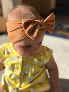 a baby girl wearing a yellow dress and a brown headband with a bow on it