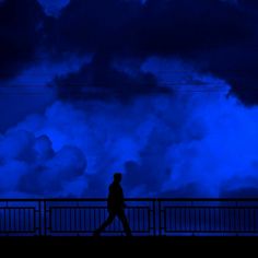 a man walking across a bridge at night with clouds in the sky behind him and power lines above