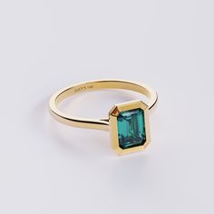 a gold ring with an emerald colored stone in the center, on a white background