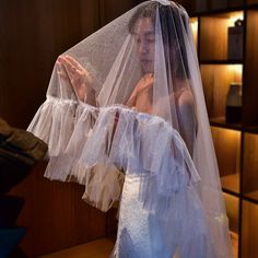 a woman wearing a white veil and dress in a room with wooden shelves on the wall