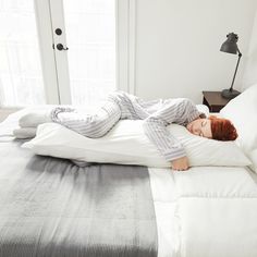 a woman laying on top of a white bed in a bedroom next to a window