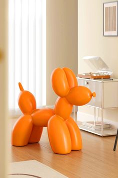 an orange balloon dog sitting on top of a wooden floor next to a white table