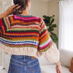 a woman wearing a multicolored sweater and jean shorts is standing in a living room