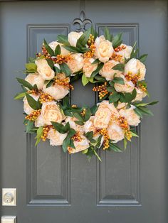 a wreath on the front door with flowers and greenery hanging from it's side