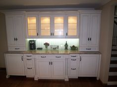 an empty kitchen with white cabinets and marble counter tops on hardwood floors in front of stairs