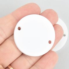 a hand holding a small white object in it's right hand with two holes