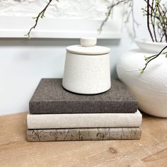 two books are stacked on top of each other next to a white vase with branches in it