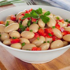 a white bowl filled with bean salad on top of a wooden cutting board next to a fork