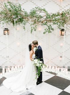 a bride and groom standing in front of a checkered floor with greenery hanging from the ceiling