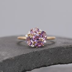 a pink and white diamond ring sitting on top of a gray stone slab with other stones surrounding it