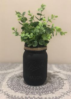 a black mason jar filled with green plants on top of a white and gray table cloth