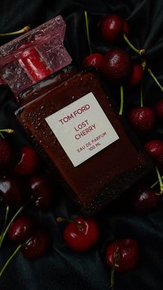 a bottle of tom ford cherry jelly next to some cherries on a black cloth