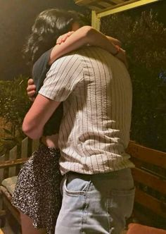 two people embracing each other in front of a mirror with plants on it and trees behind them