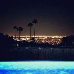 the city lights are visible in the distance from an outdoor swimming pool with palm trees