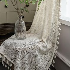 a white crocheted tablecloth draped over a glass vase filled with green leaves