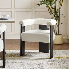 a white chair sitting on top of a rug next to a table with a potted plant