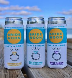 three cans of bride moon party and drink on a wooden table near the ocean with blue sky in background