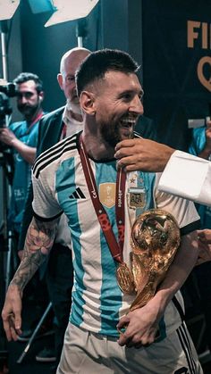 a man holding a soccer trophy in his right hand and smiling at the camera while another man stands behind him