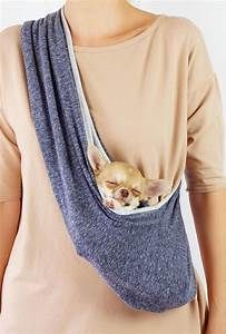 a woman holding a small dog in a sling