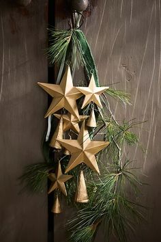 an origami star decoration hanging from a wooden door with pine needles and bells