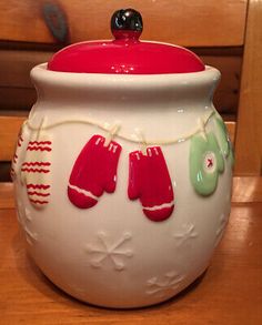 a white ceramic jar with red and green mittens on the lid sitting on a wooden table