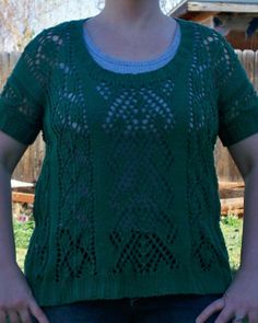 a woman standing in front of a fence with her hands on her hips, wearing a green sweater