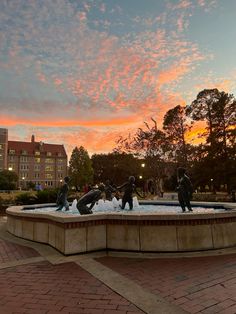 some people are playing around in the water fountain at sunset or dawn with buildings in the background