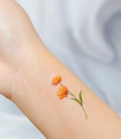 a small flower tattoo on the wrist is shown in oranges and yellows with green leaves