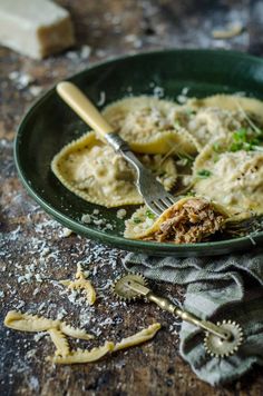 a green bowl filled with pasta and meat on top of a wooden table next to silverware